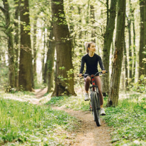 Beautiful woman bicycle outdoors. Girl in a summer forest.